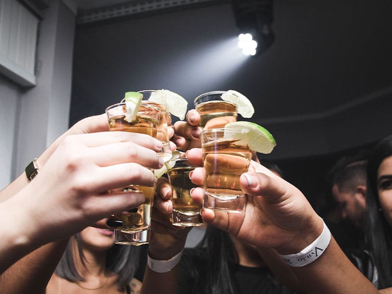 group of people hold up shots of dark liquor
