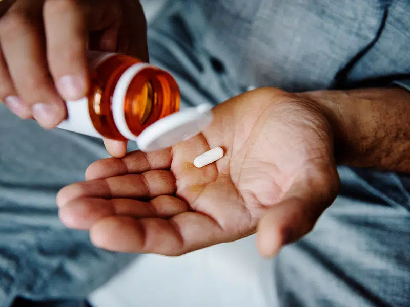 man getting a pill out of a bottle to treat alcoholism