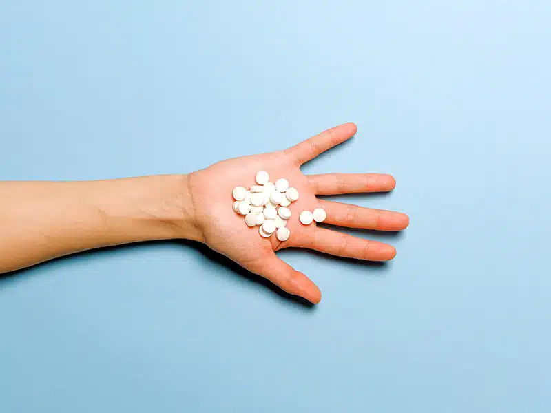 hand holding white pills on a blue background