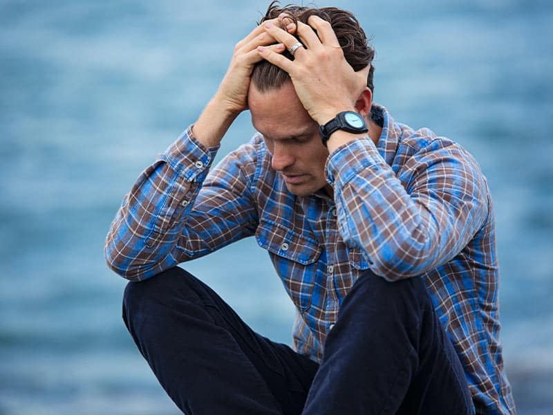 man outside grasping his head visibly stressed out